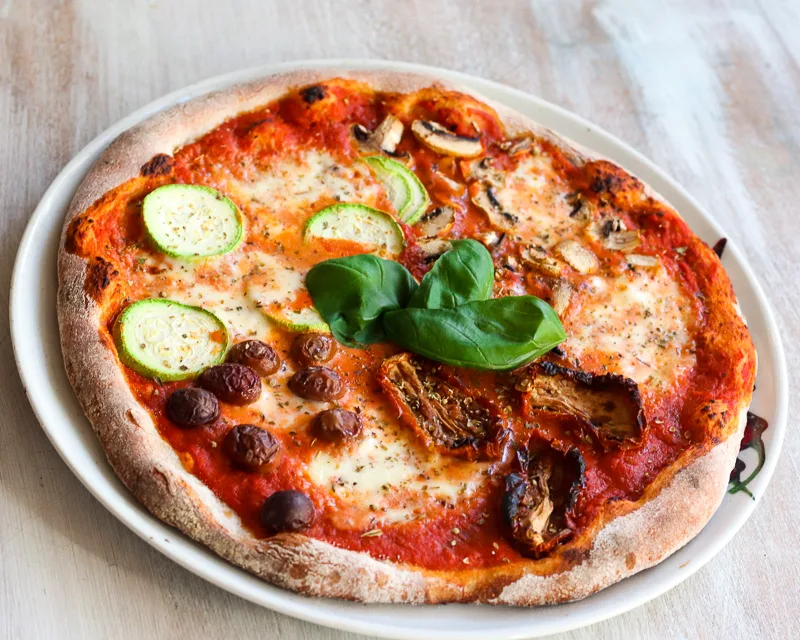 Steinofenpizza mit Zucchini, Oliven, getrockneten Tomaten und frischem Basilikum